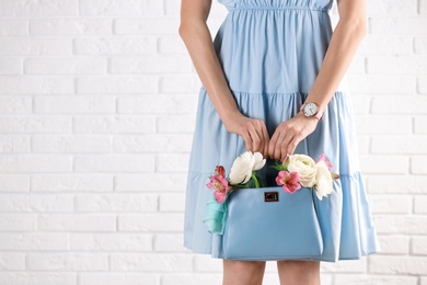 Photo of Woman holding elegant handbag with spring flowers against white brick wall, closeup. Space for text