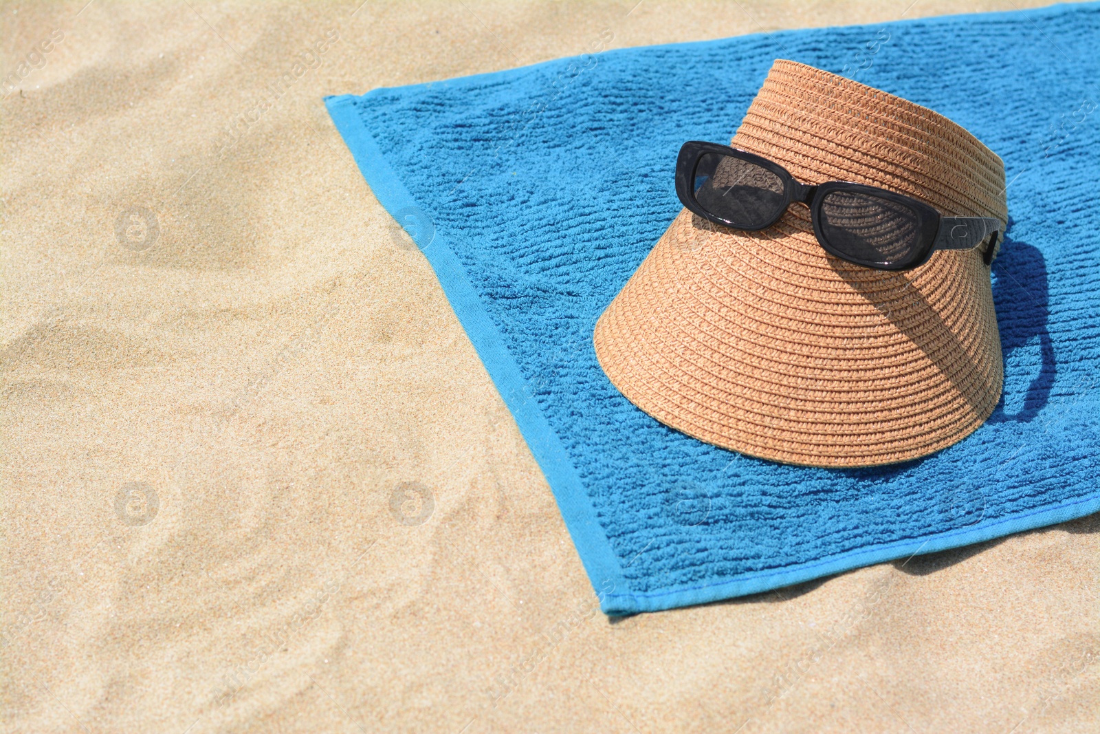 Photo of Towel, straw visor cap and sunglasses on sand, space for text. Beach accessories