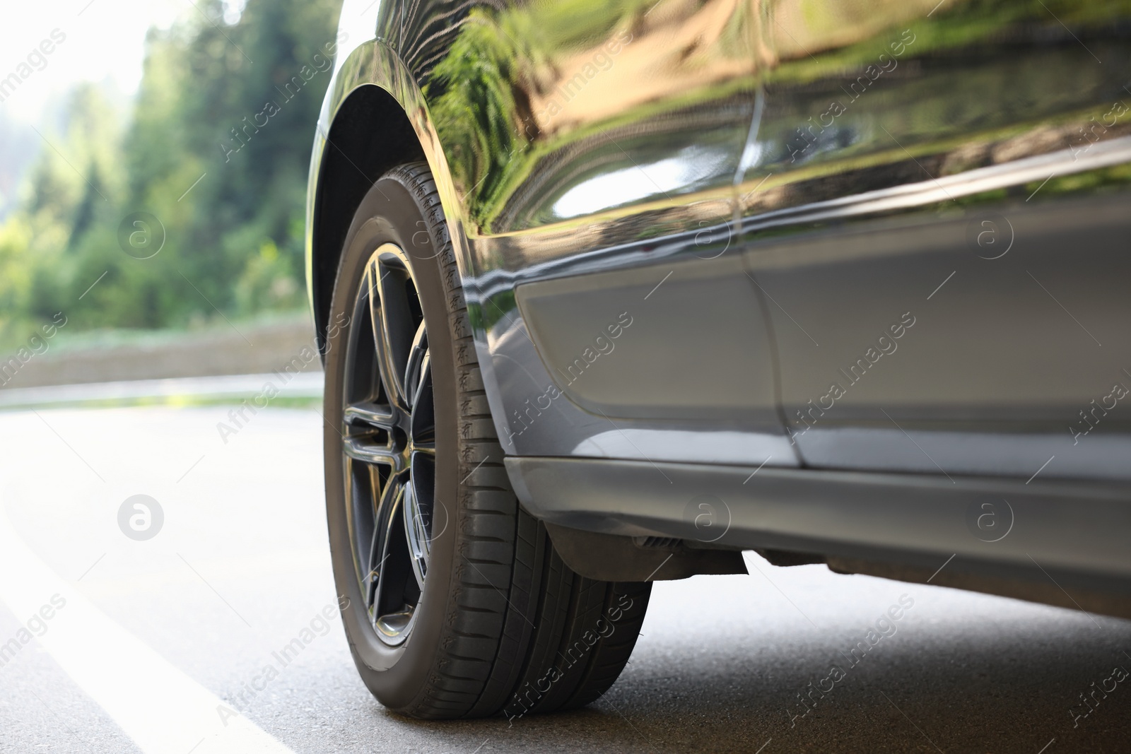 Photo of Modern black car on asphalt road outdoors, closeup. Space for text