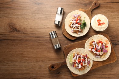 Delicious tacos with vegetables, meat and sauce on wooden table, flat lay. Space for text