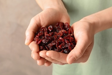 Woman holding handful of tasty cranberries on color background, closeup. Dried fruits as healthy snack