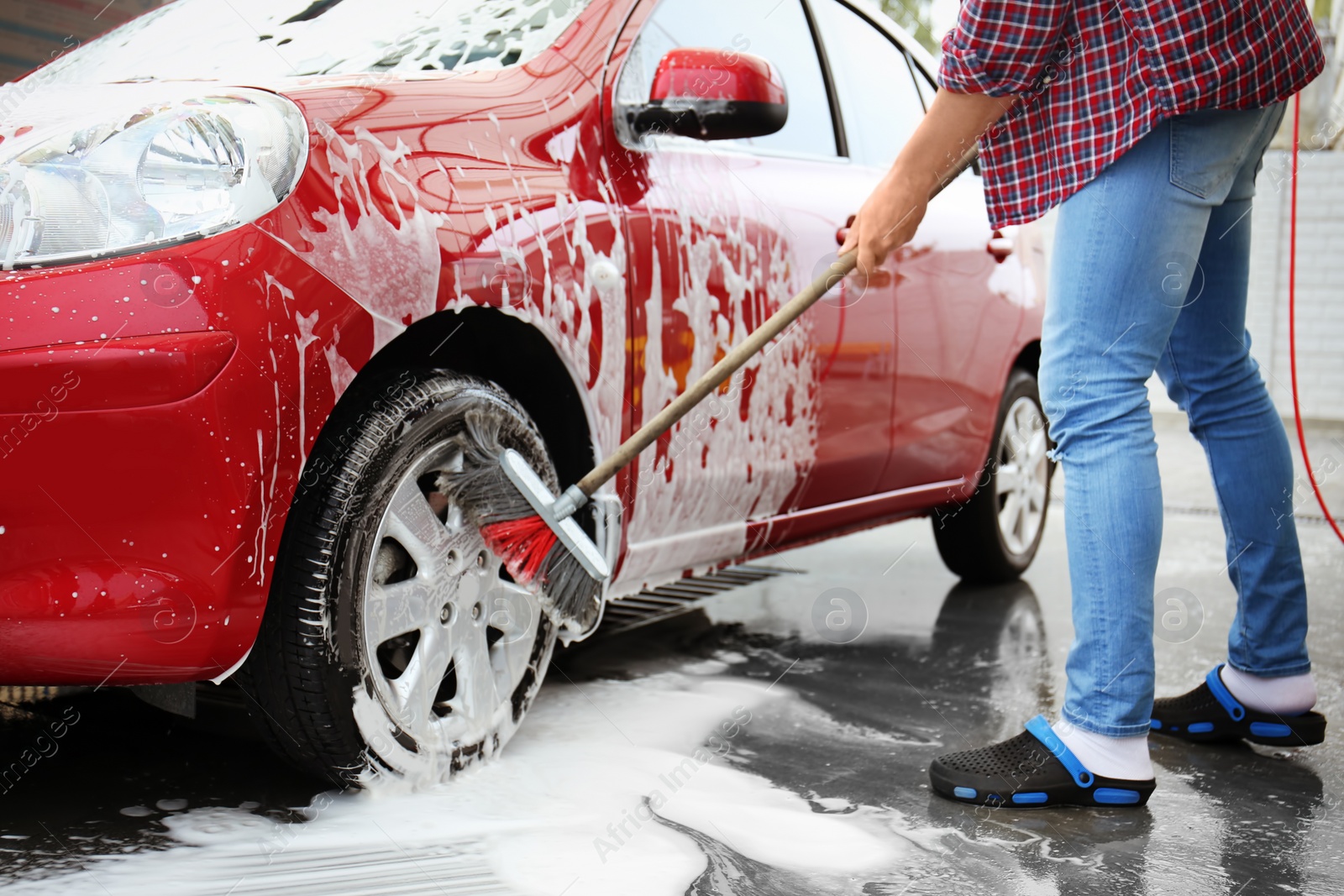 Photo of Young man cleaning vehicle with brush at self-service car wash