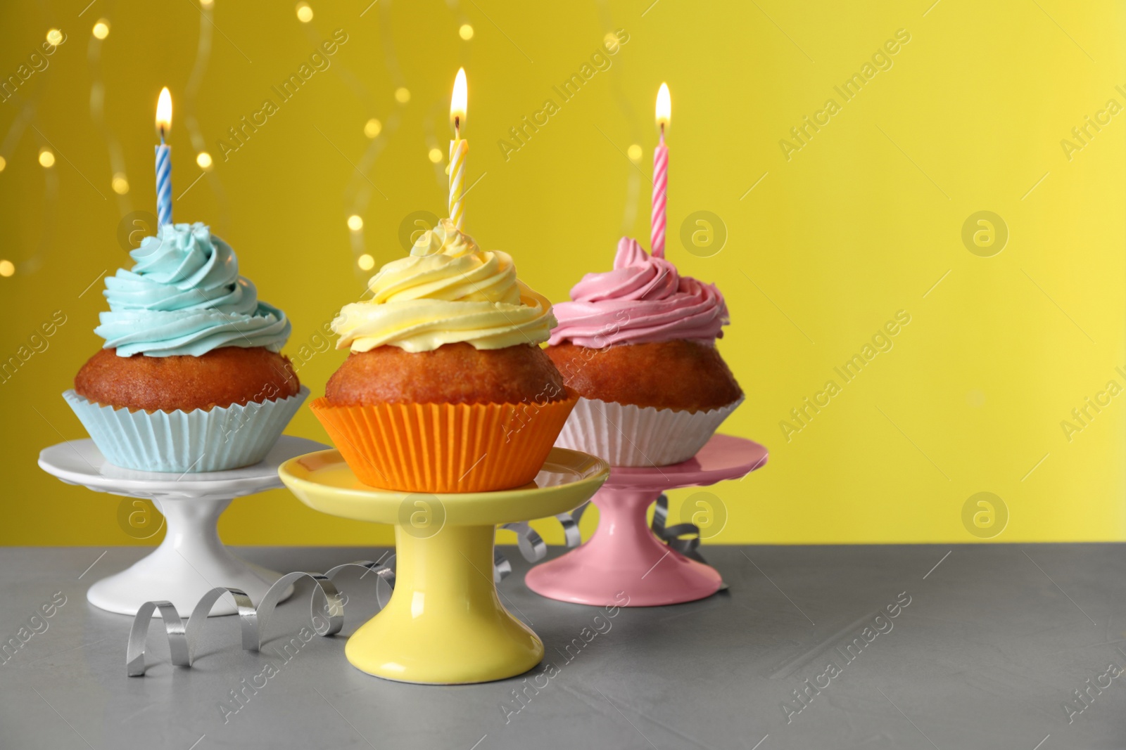 Photo of Delicious birthday cupcakes with candles on white table against blurred festive lights