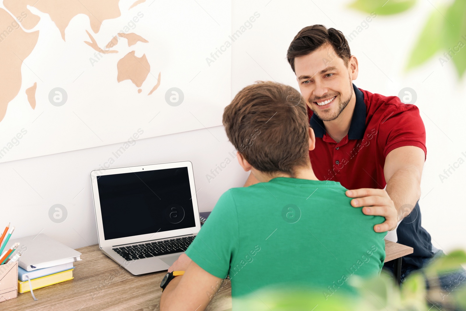 Photo of Father helping his teenager son with homework indoors