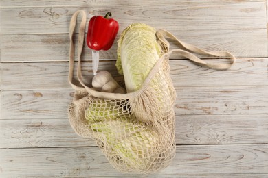 Photo of Fresh Chinese cabbage, bell pepper and garlic in net bag on wooden table, top view