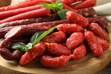 Photo of Different thin dry smoked sausages and basil on wooden board, closeup