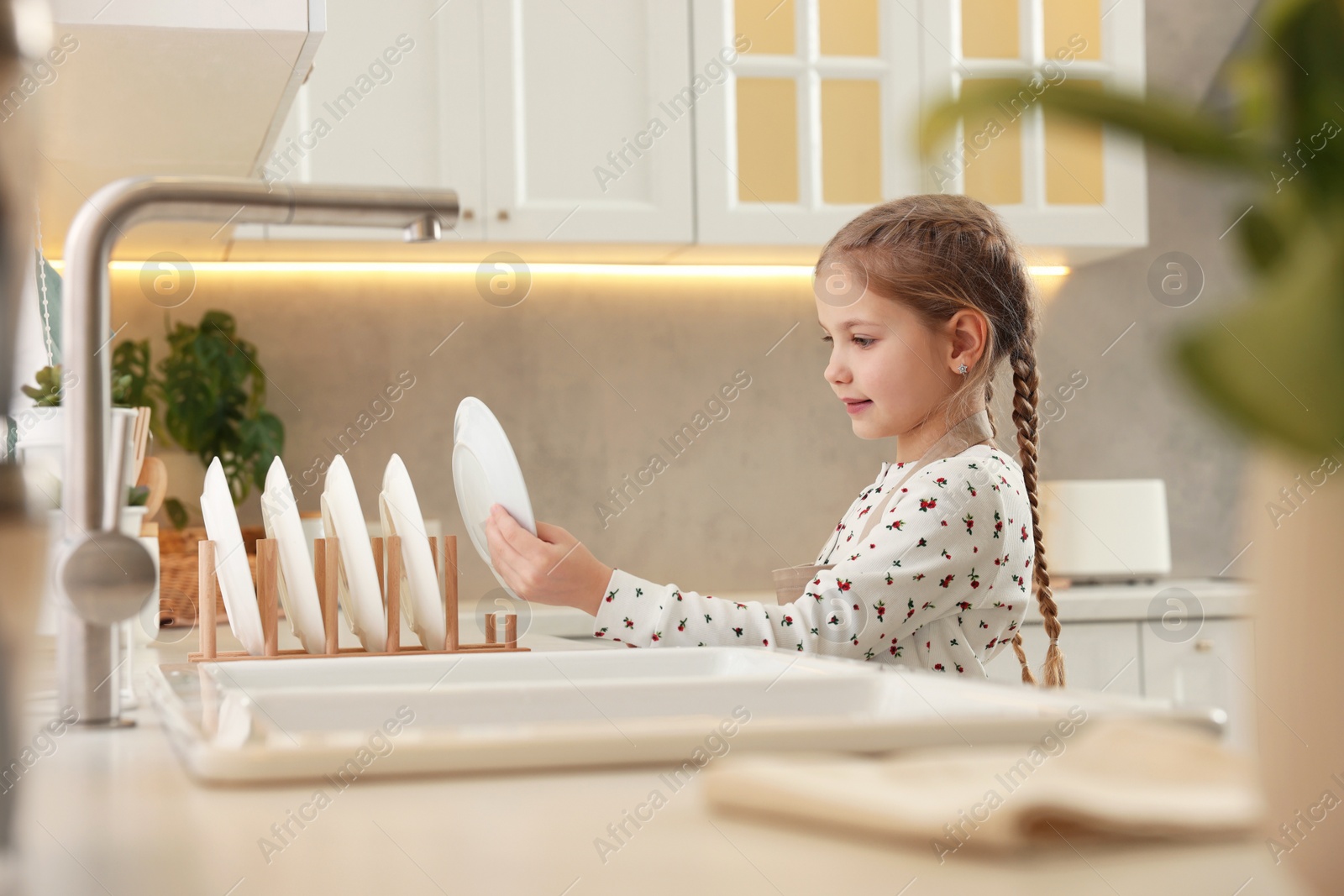 Photo of Girl putting clean plate on drying rack in kitchen