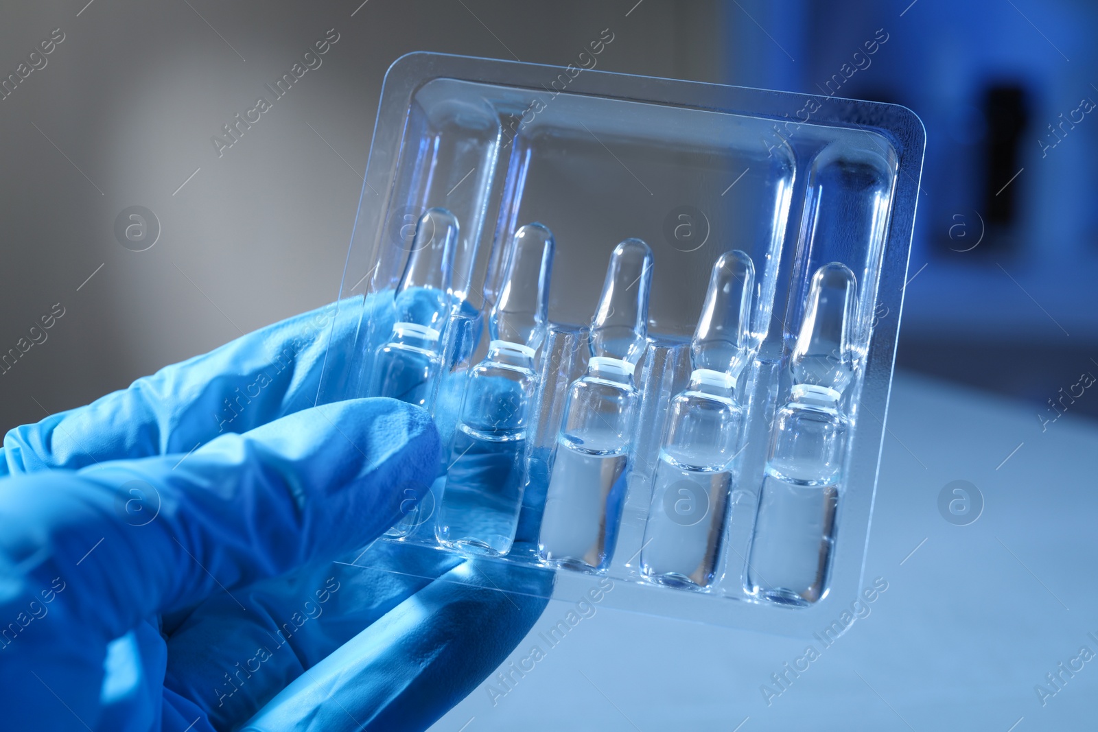 Photo of Doctor holding tray with ampoules on blurred background, closeup