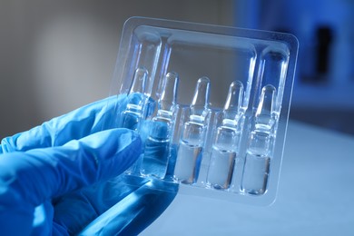 Doctor holding tray with ampoules on blurred background, closeup
