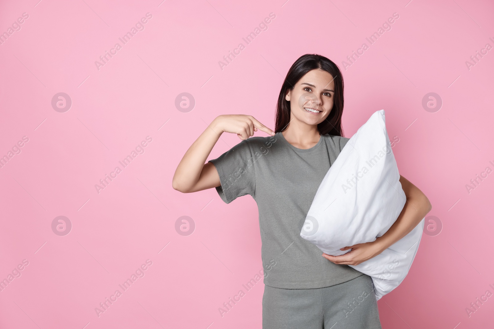 Photo of Happy young woman pointing at soft pillow on pink background, space for text