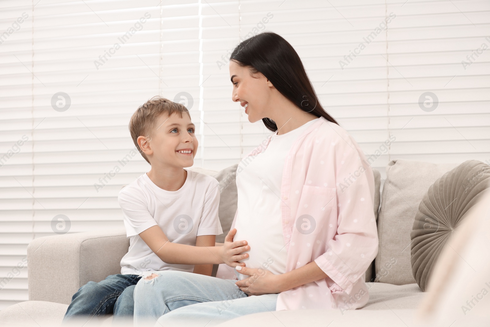 Photo of Cute boy touching pregnant mother's belly at home