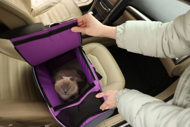 Photo of Woman closing pet carrier with cat in car, closeup
