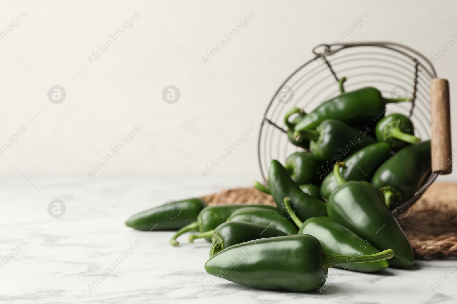 Photo of Green chili peppers and metal basket on marble table. Space for text