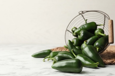 Photo of Green chili peppers and metal basket on marble table. Space for text