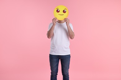Photo of Man covering face with smiling emoticon on pink background