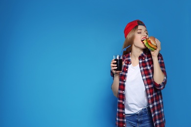 Pretty woman with tasty burger and cola on color background. Space for text