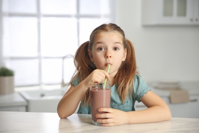 Photo of Cute little child drinking tasty chocolate milk in kitchen