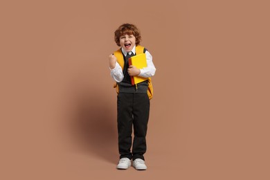 Emotional schoolboy with backpack and books on brown background