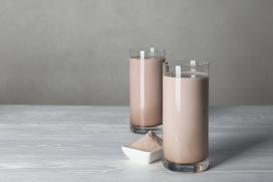 Glasses with protein shake and bowl of powder on white wooden table. Space for text