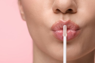 Woman with beautiful lip gloss and applicator on pink background, closeup