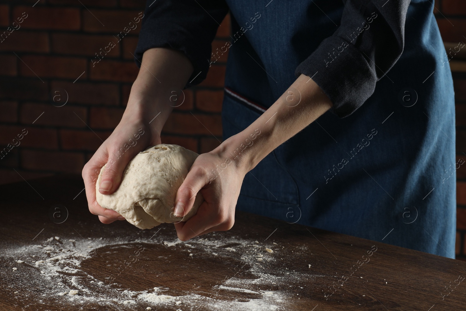 Photo of Making bread. Woman kneading dough at wooden table indoors, closeup