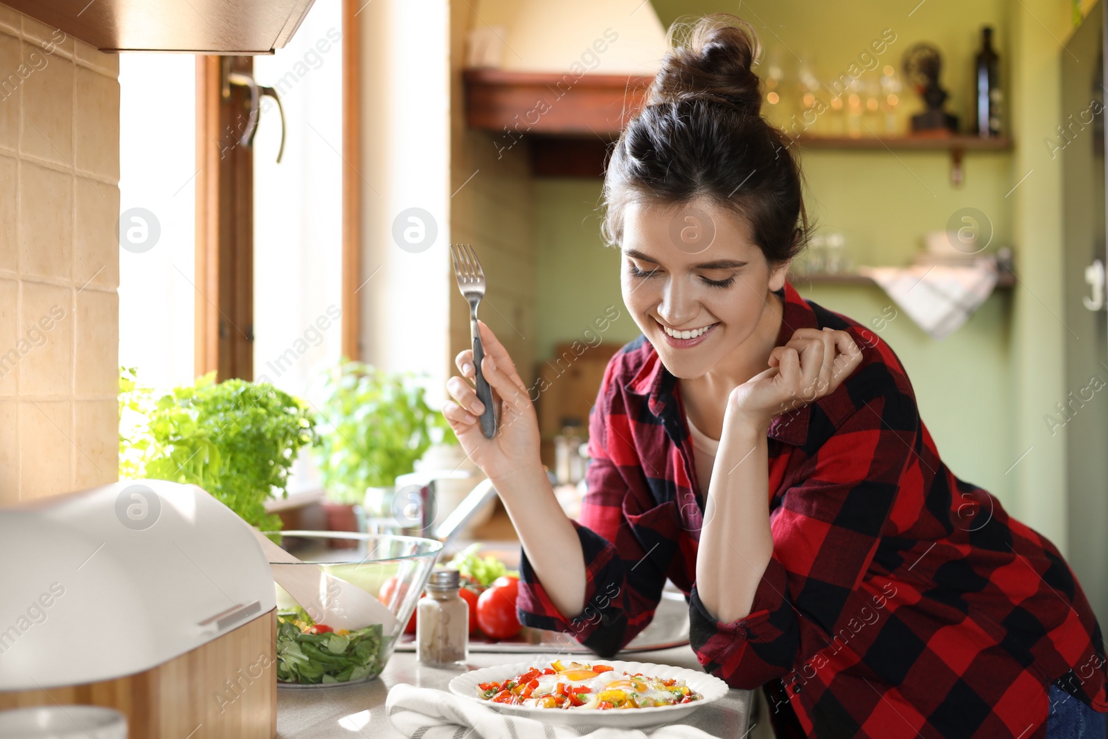 Photo of Young woman with plate of freshly fried eggs and vegetables at countertop in kitchen