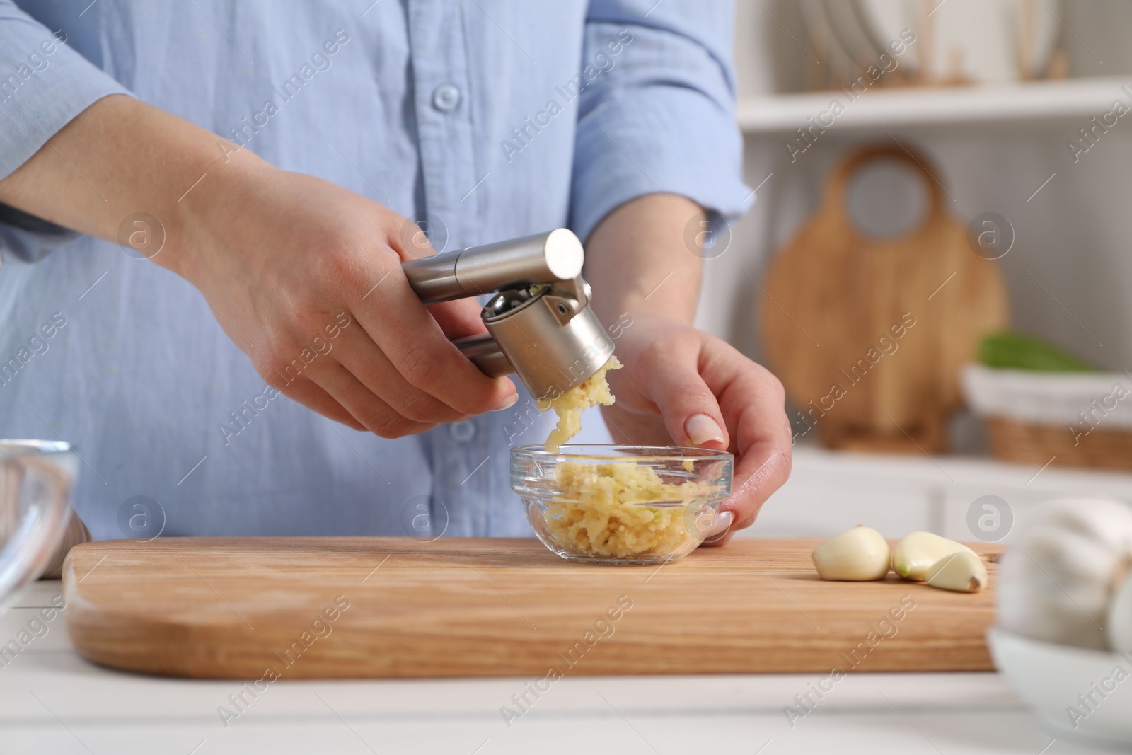 Photo of Woman squeezing garlic with press at white table in kitchen, closeup