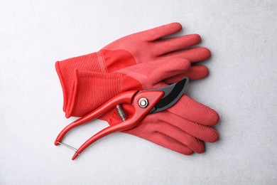 Photo of Pair of red gardening gloves and secateurs on light grey table, top view