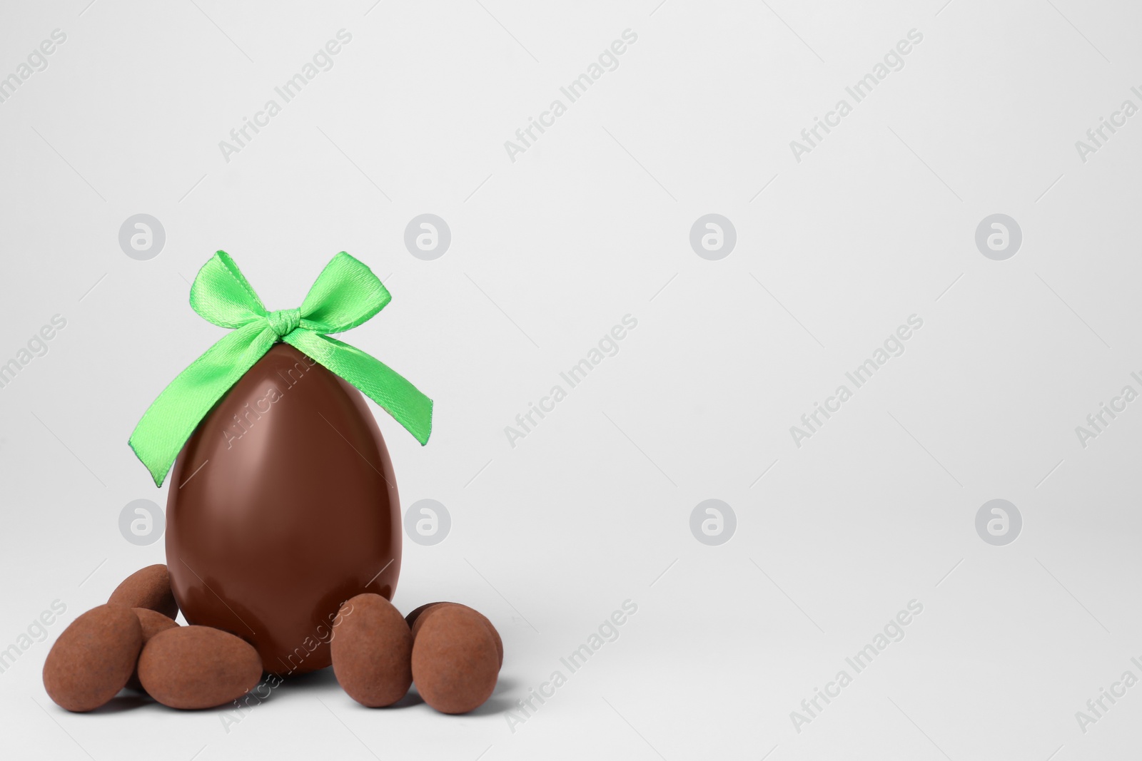 Photo of Tasty chocolate egg with green bow and candies on light background, space for text