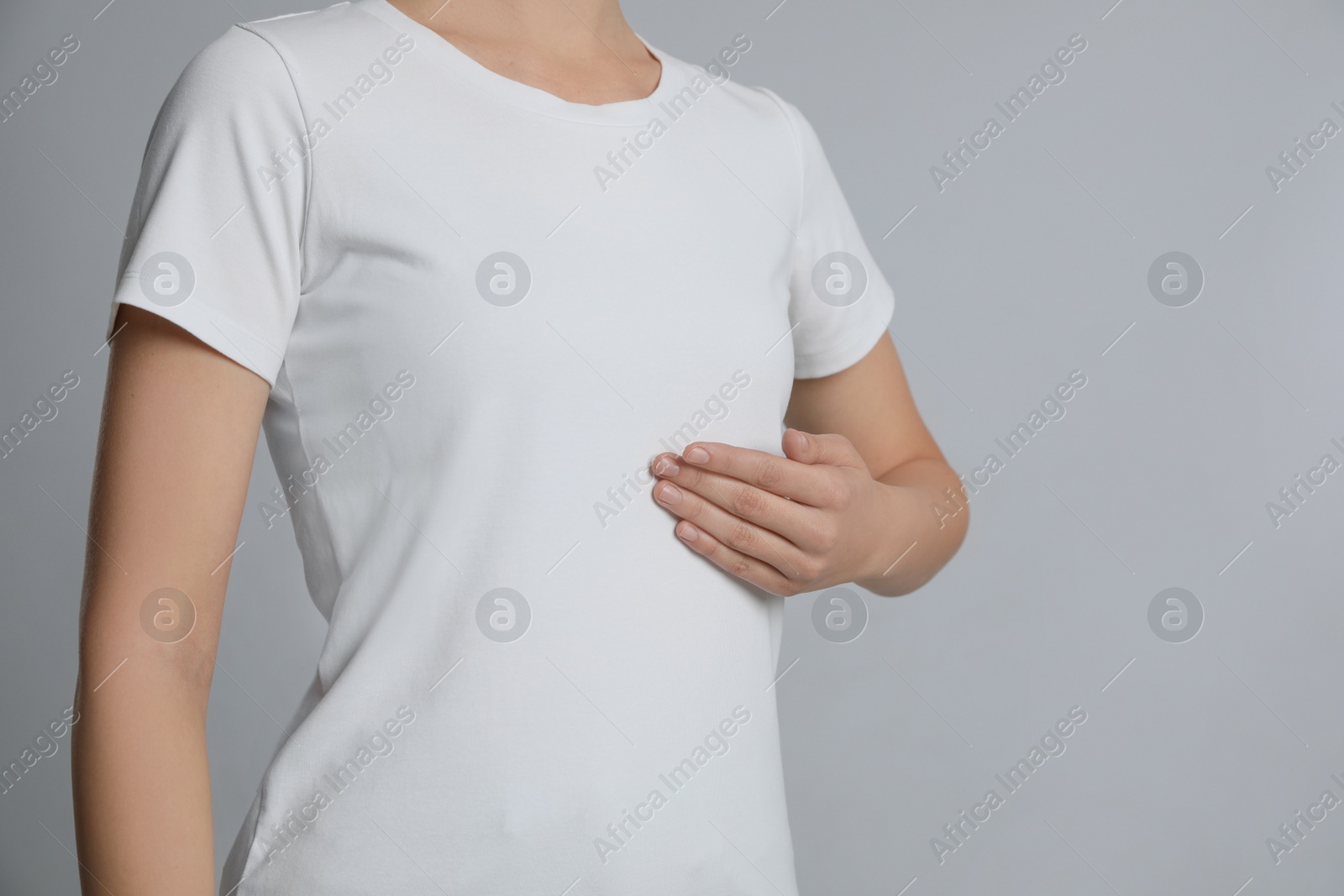 Photo of Woman holding hand near chest on light grey background, closeup