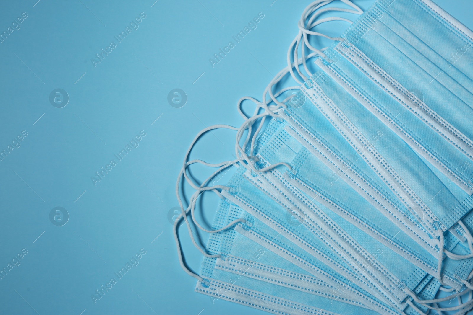 Photo of Disposable face masks on light blue background, flat lay with space for text. Protective measures during coronavirus quarantine