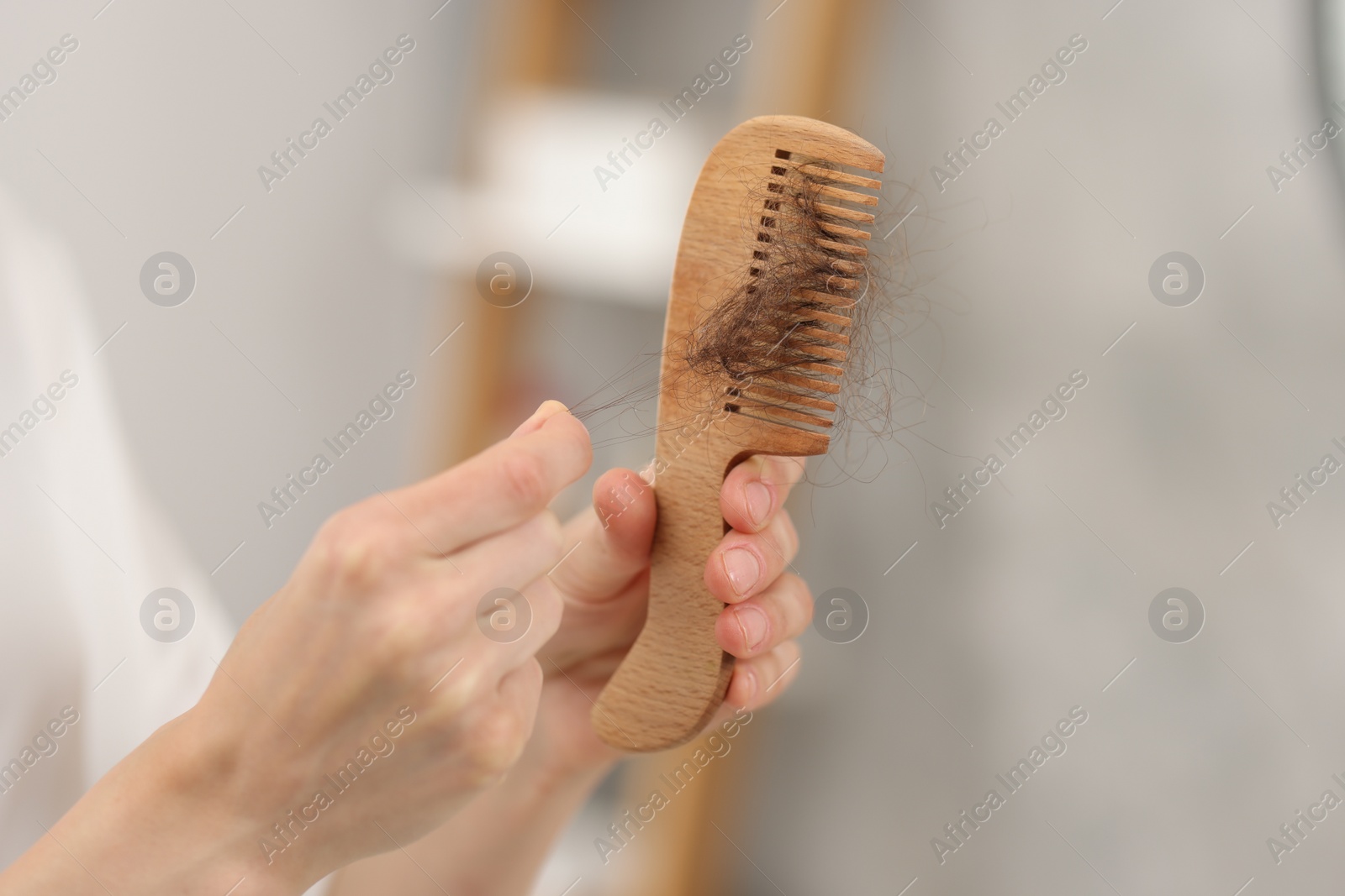 Photo of Woman taking her lost hair from comb at home, closeup. Alopecia problem