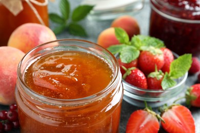 Jars with different jams and fresh fruits on table, closeup