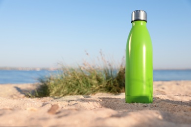 Photo of Modern green thermos bottle on beach. Space for text
