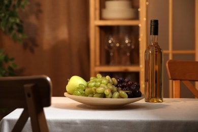 Photo of Bottle of wine and plate with ripe fruits on table indoors