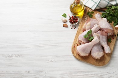 Raw chicken drumsticks and ingredients on white wooden table, flat lay. Space for text