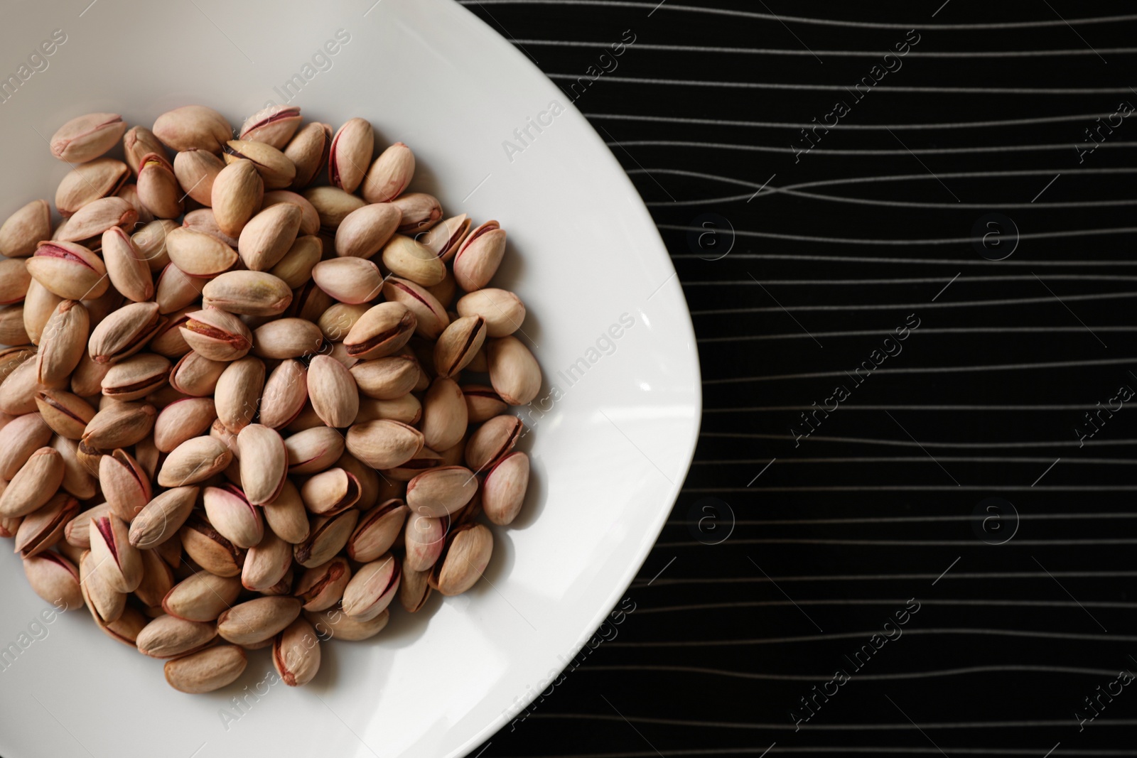 Photo of Many tasty pistachios on black table, top view. Space for text