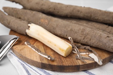 Photo of Raw salsify roots and peeler on white table, closeup