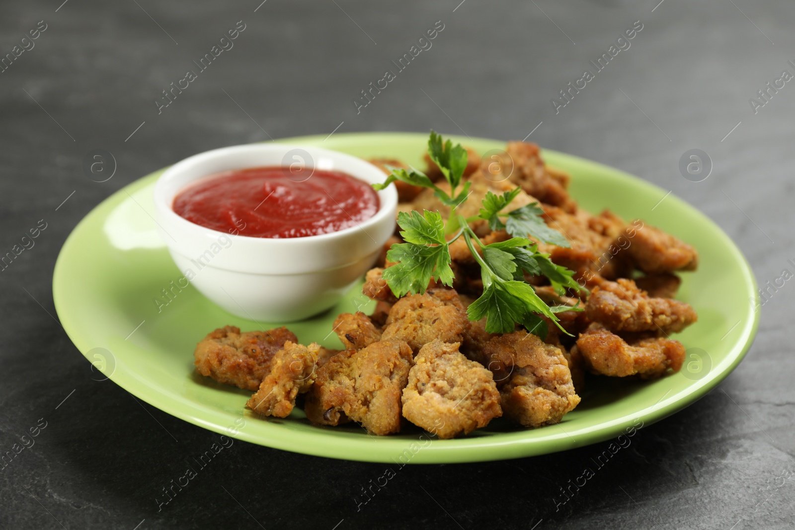 Photo of Delicious cooked soy meat chunks with sauce black slate table, closeup