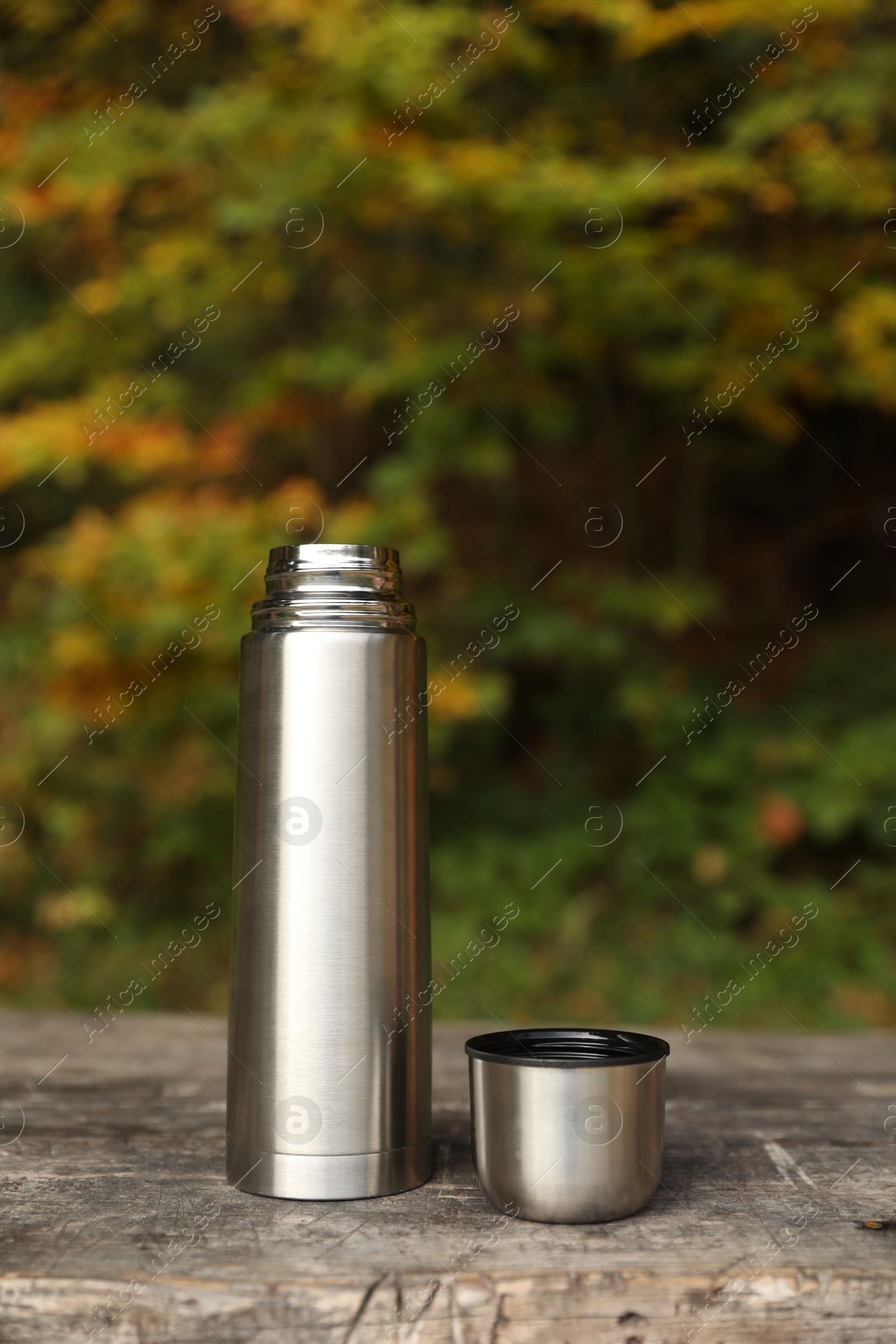 Photo of Metallic thermos and cup lid on wooden bench outdoors