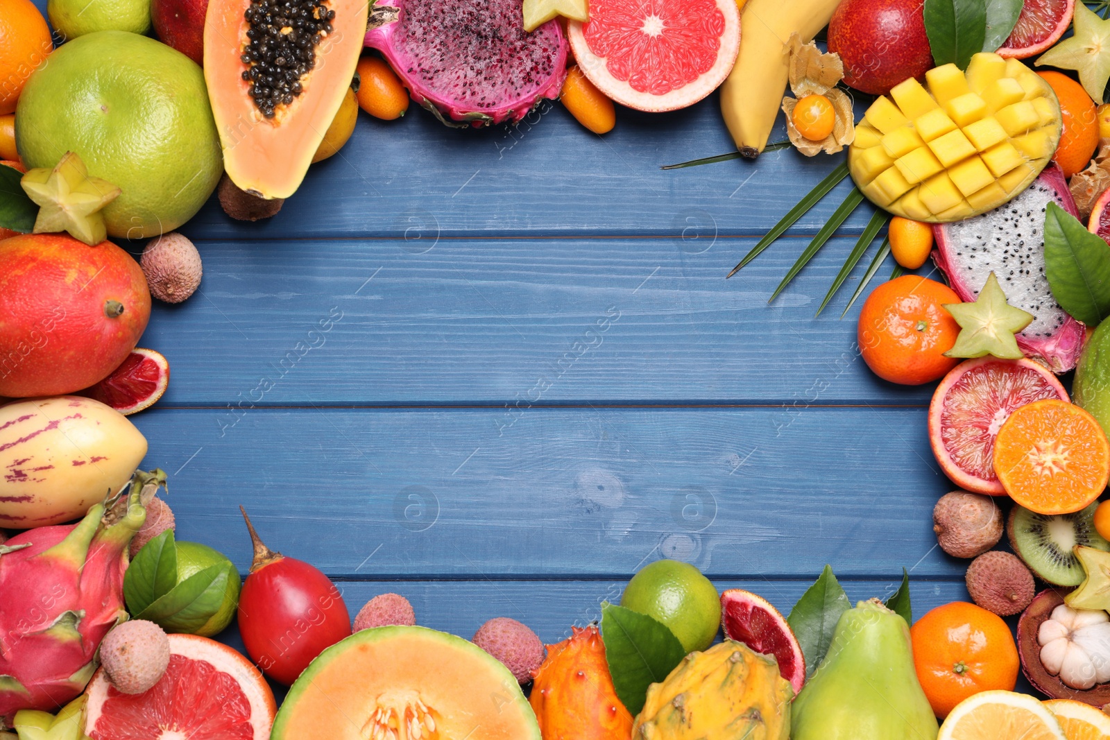 Photo of Frame of different exotic fruits on blue wooden background, flat lay. Space for text