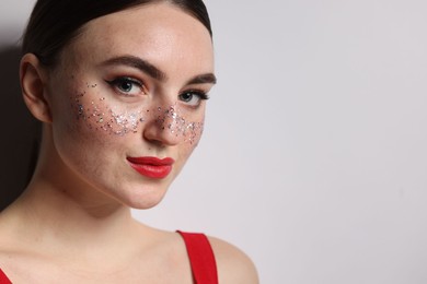 Beautiful woman with glitter freckles on light background. Space for text