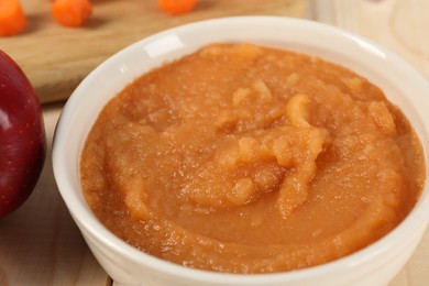 Photo of Healthy baby food. Bowl with delicious carrot puree on wooden table, closeup