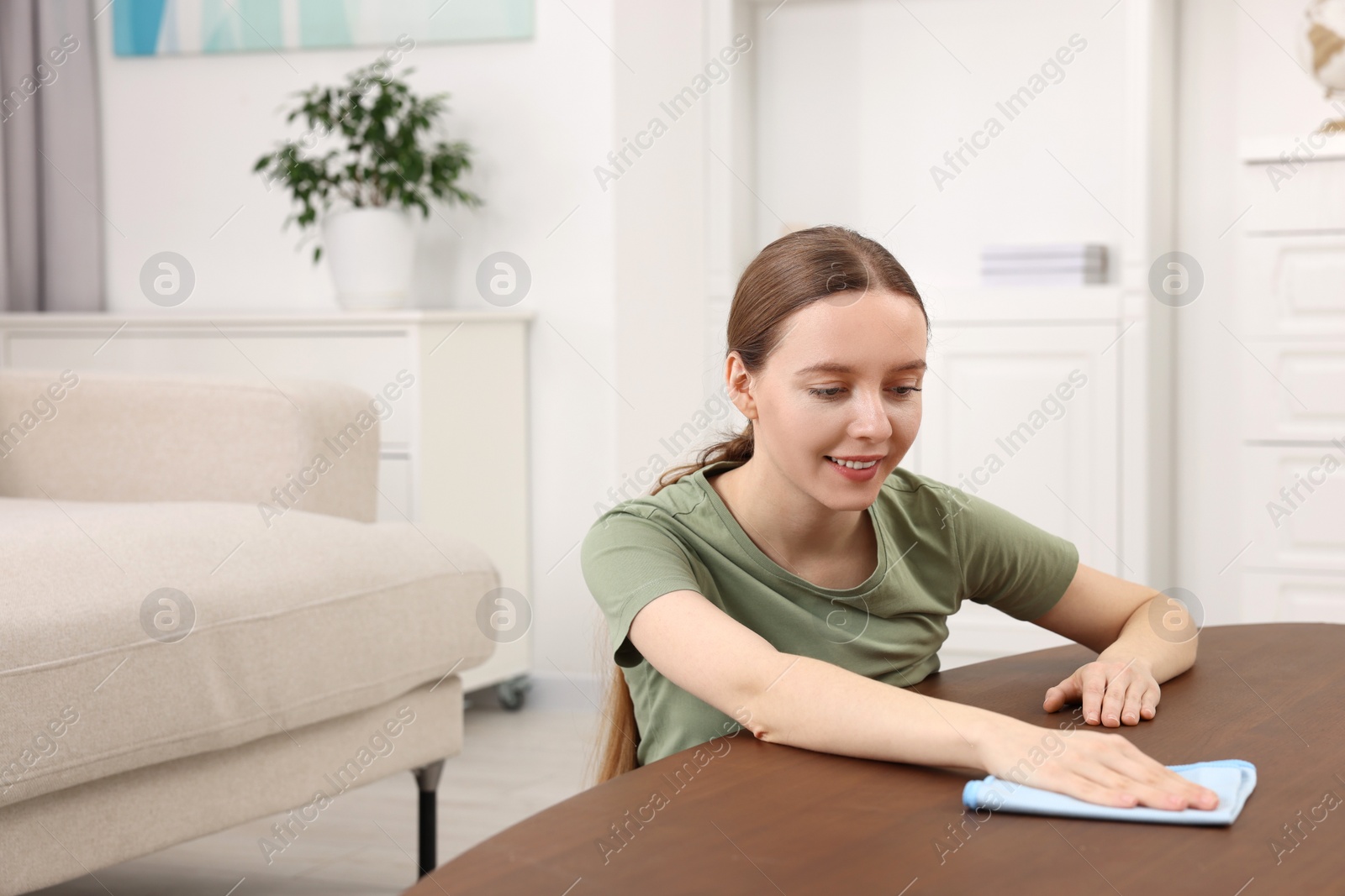 Photo of Woman with microfiber cloth cleaning wooden table in room