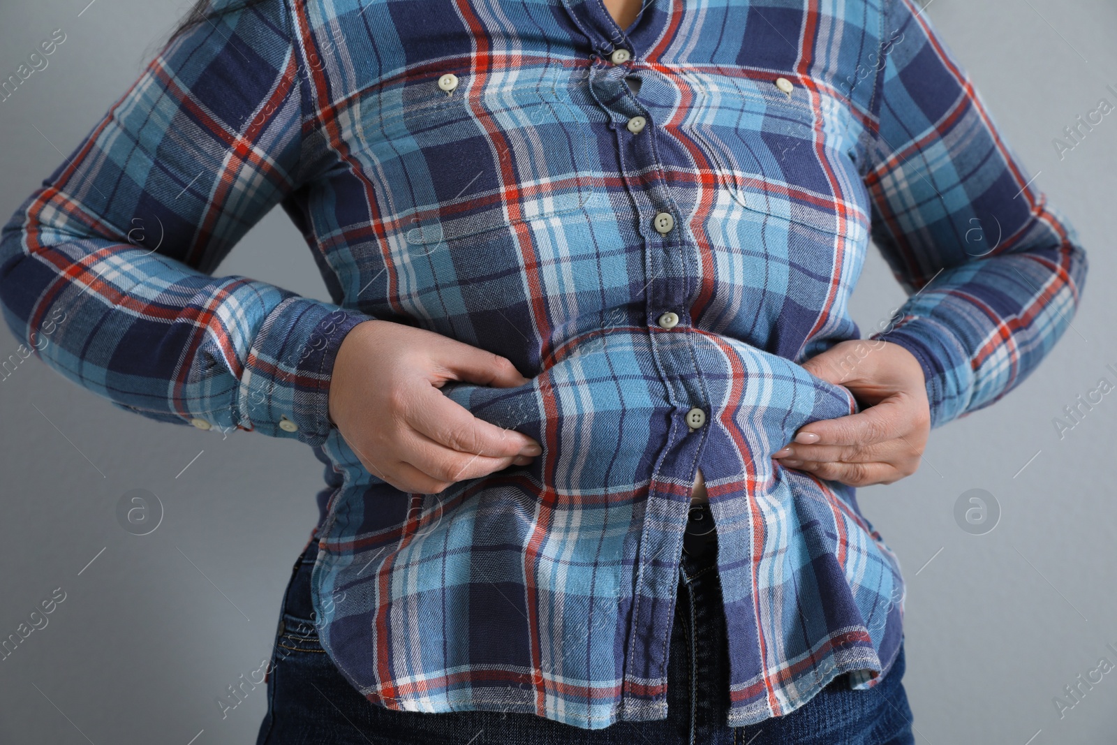 Photo of Overweight woman in tight shirt on light grey background, closeup