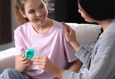 Photo of Mother giving condom to her teenage daughter at home. Sex education concept