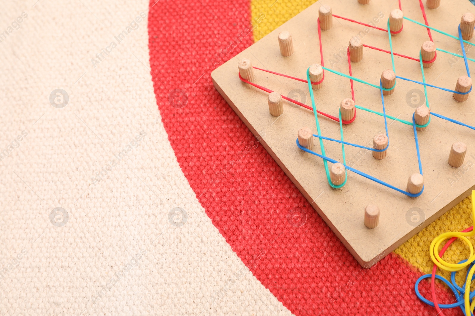 Photo of Wooden geoboard with rubber bands on carpet, space for text. Motor skills development