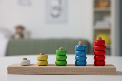 Photo of Motor skills development. Stacking and counting game wooden pieces on white table indoors, closeup