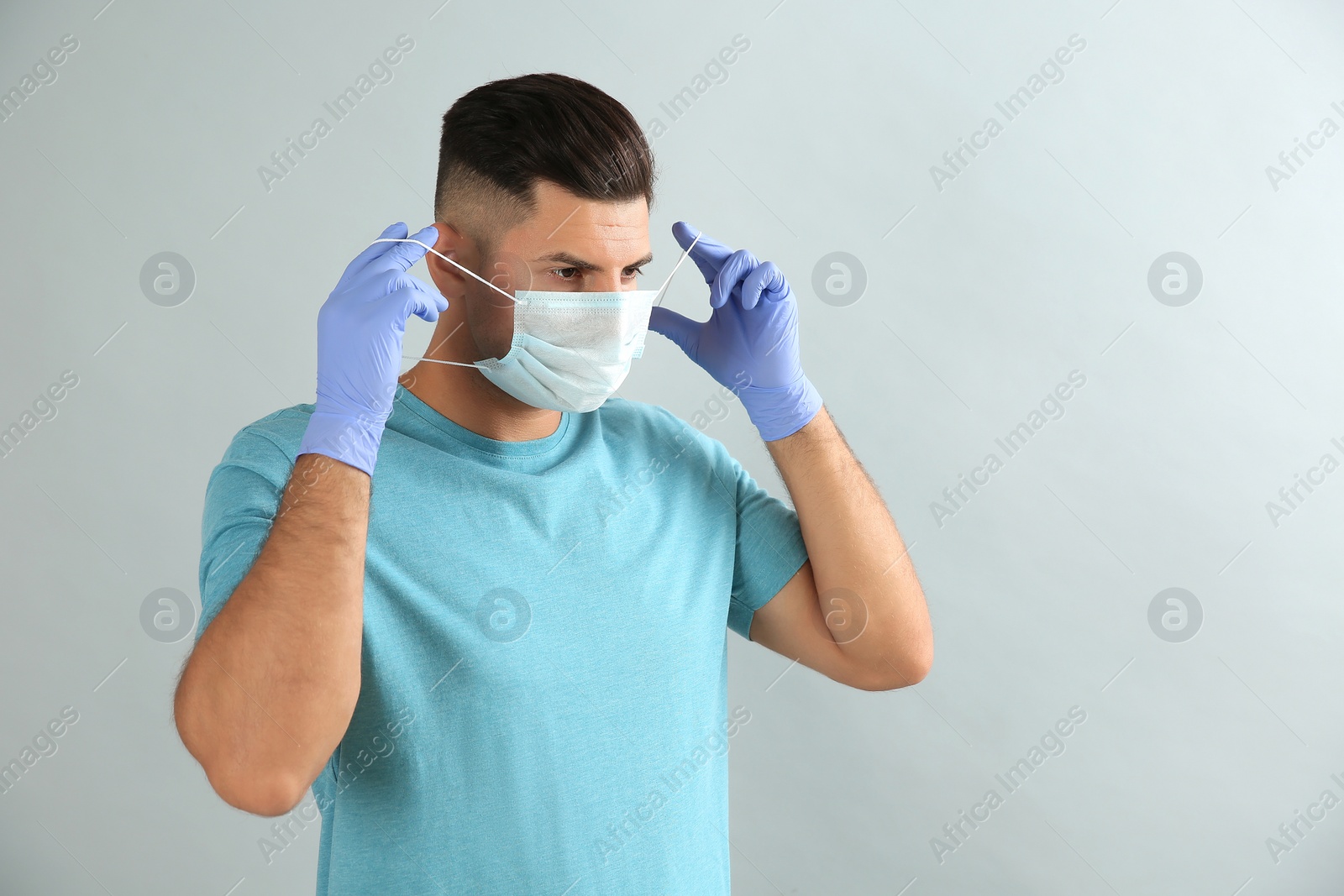 Photo of Man in medical gloves putting on protective face mask against grey background
