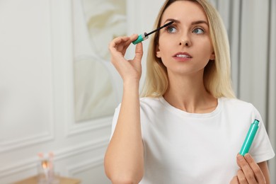 Photo of Beautiful woman applying mascara at home, space for text